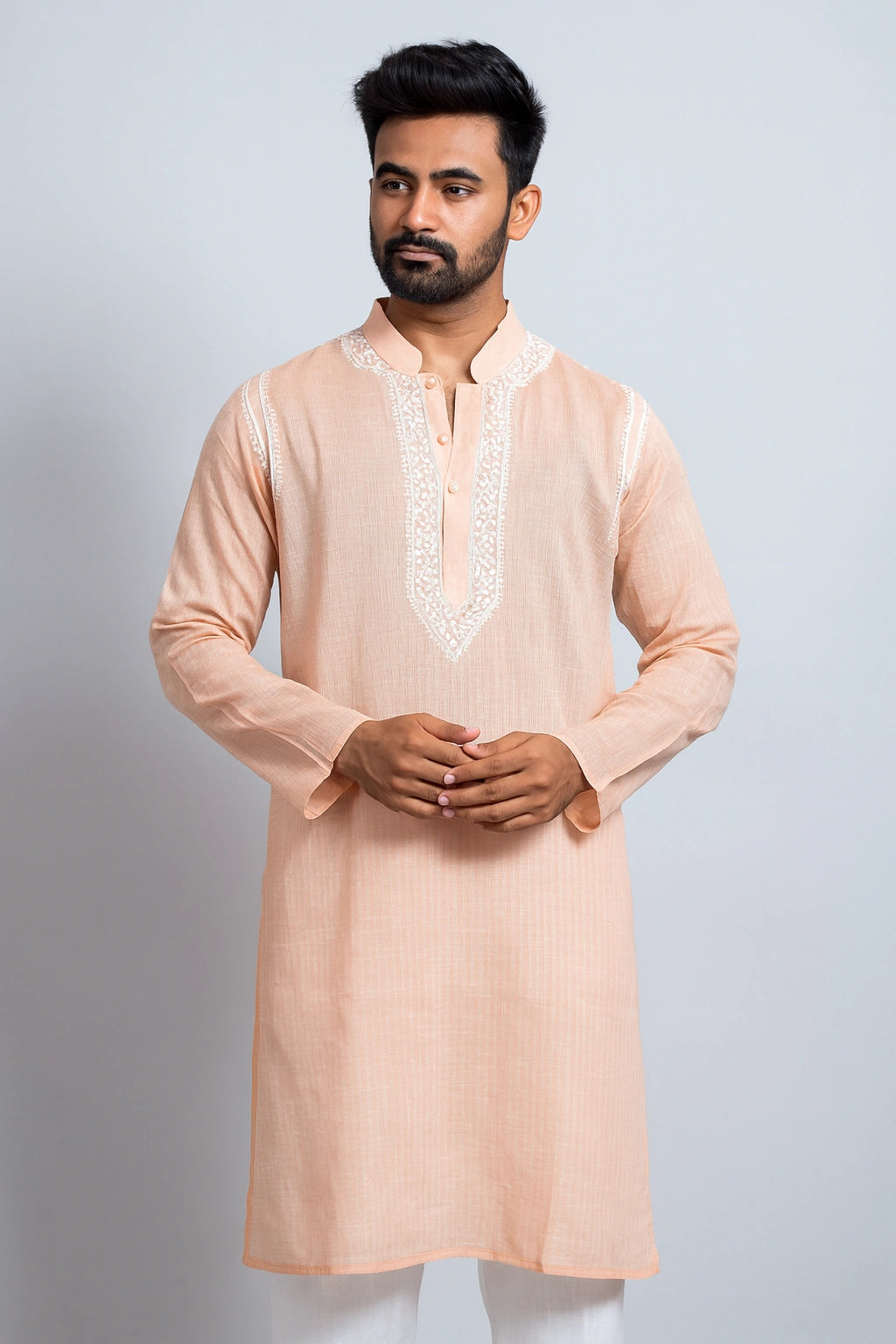 Man wearing a peach kurta with white embroidery on a light gray background