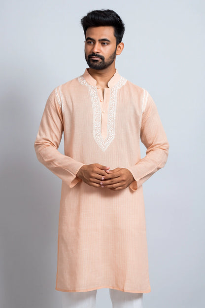 Man wearing a peach kurta with white embroidery on a light gray background