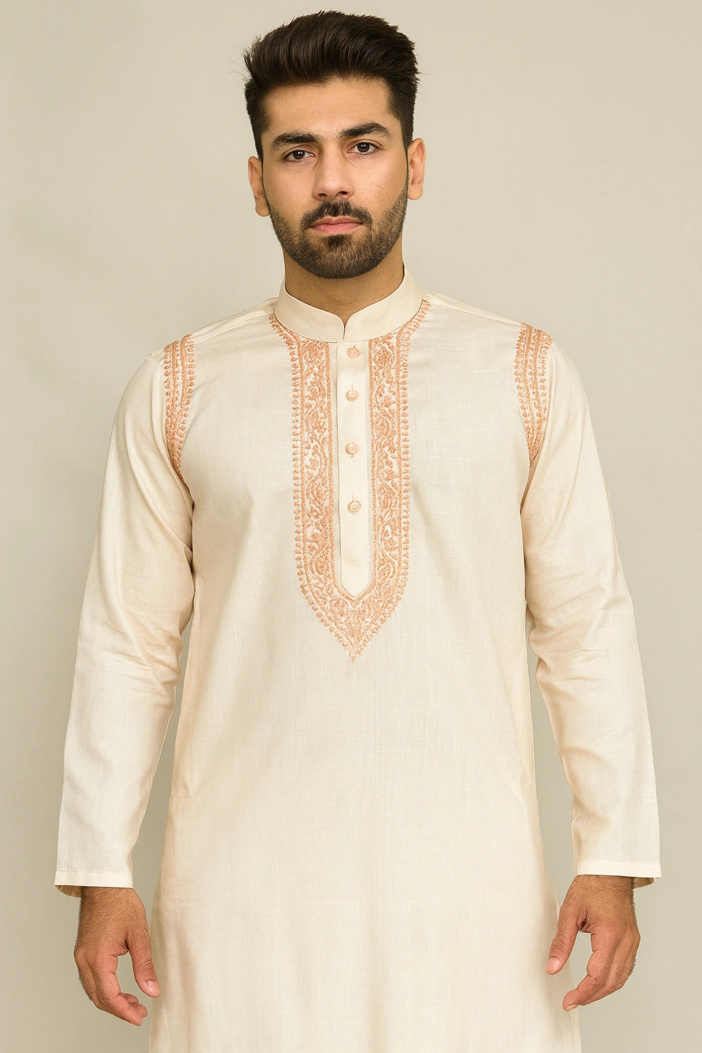 Man wearing a cream kurta with intricate orange embroidery on a plain background