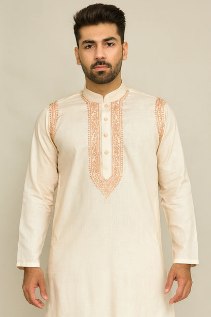 Man wearing a cream kurta with intricate orange embroidery on a plain background