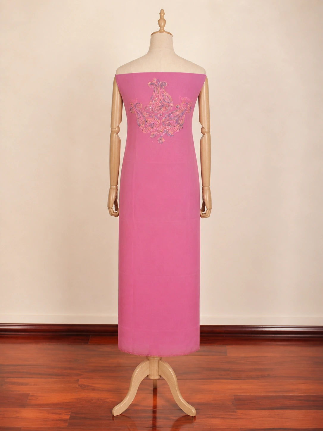 Pink evening gown with floral embroidery on a mannequin against a beige wall.