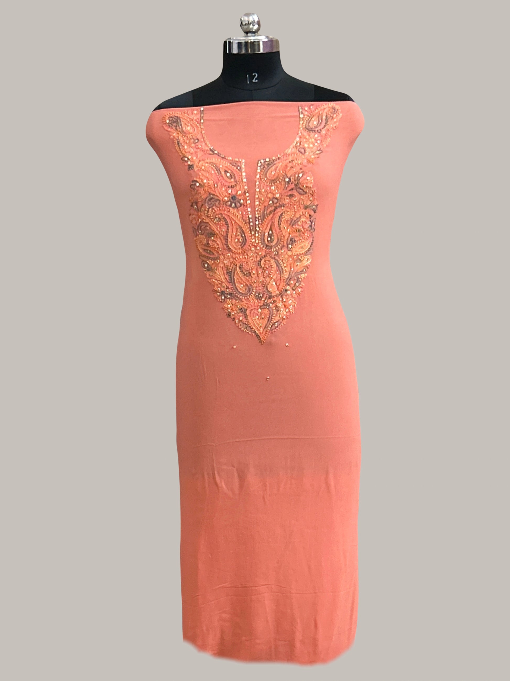 Peach dress with floral patterns on a mannequin against a gray wall with decorative panels.