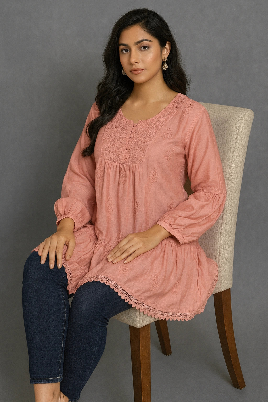 Woman wearing a lucknowi chikankari pink dress sitting on a chair against a gray background