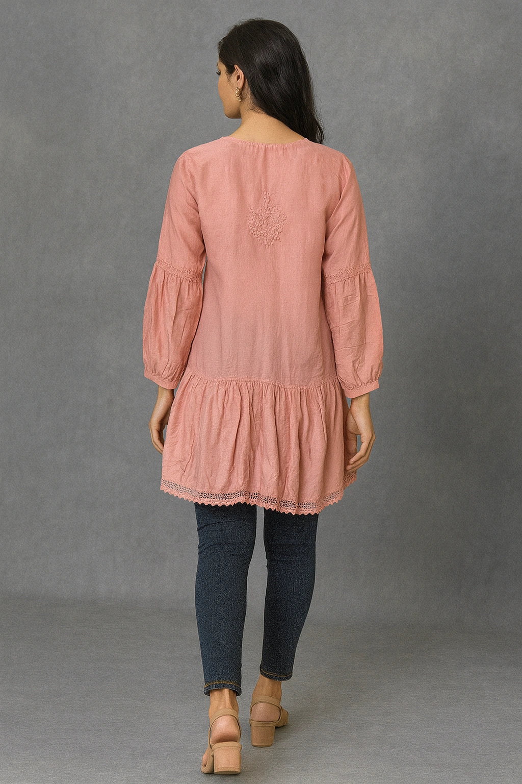 Woman wearing a lucknowi chikankari pink long-sleeve top and dark pants against a gray background