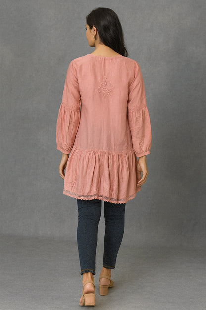 Woman wearing a lucknowi chikankari pink long-sleeve top and dark pants against a gray background