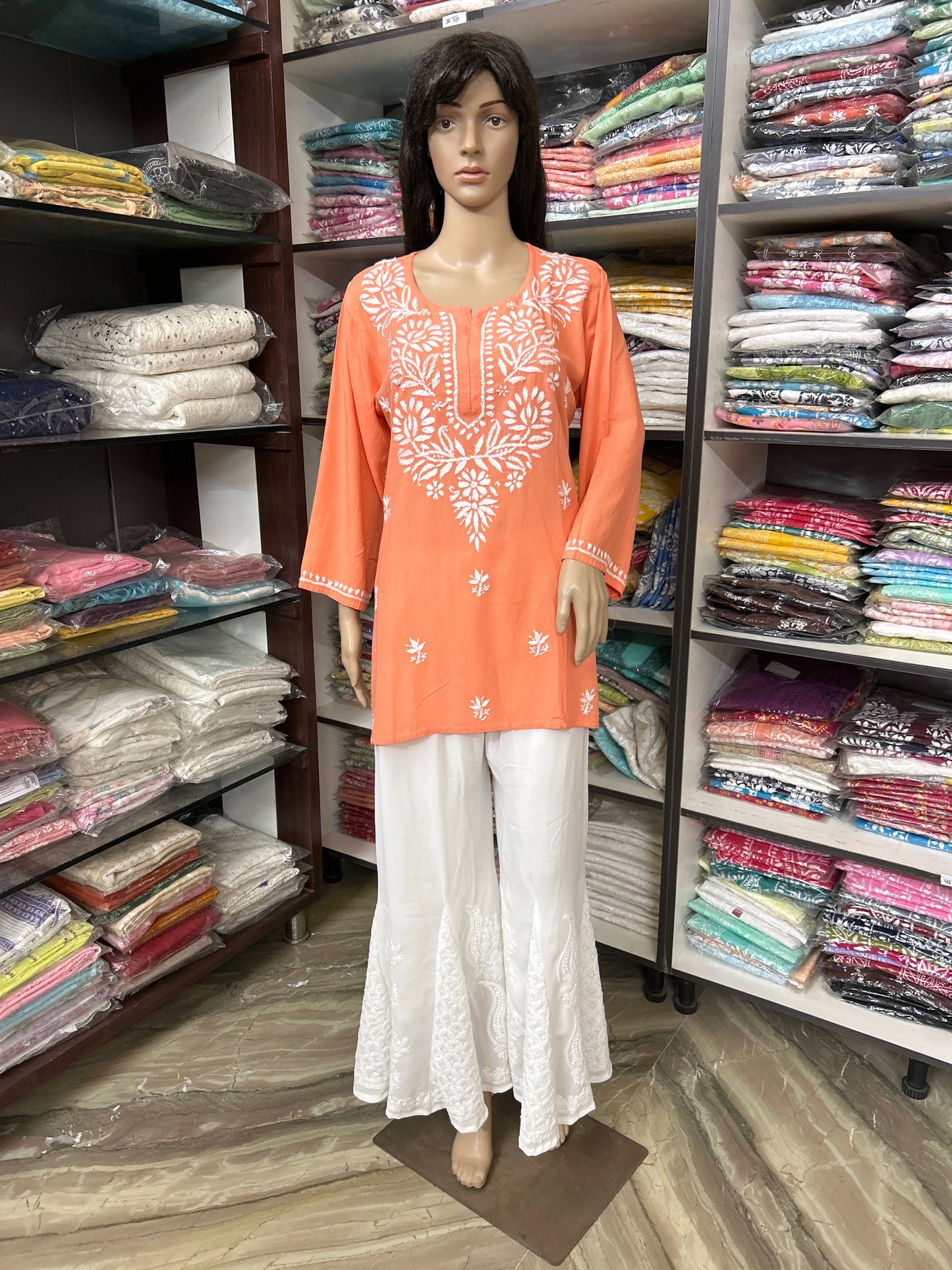 Mannequin wearing an orange embroidered top and white pants in a fabric store.