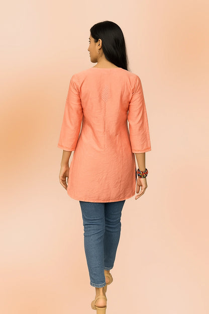 lucknowi chikankari Woman wearing a peach-colored kurta with blue jeans on a peach background