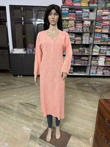 lucknowi chikankari A light peach long kurta with a subtle white floral pattern, displayed on a female mannequin in a clothing store. The mannequin is standing in front of shelves filled with folded garments.