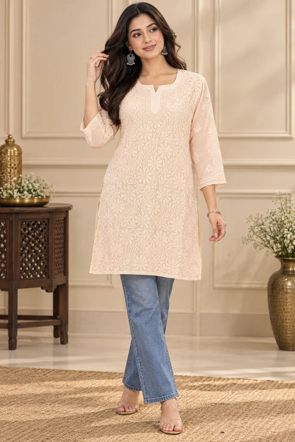 Woman wearing a lucknowi chikankari  peach kurta with white floral patterns 