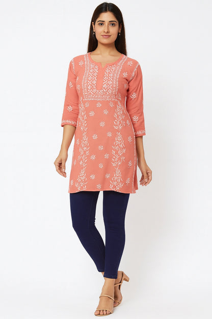Woman wearing a lucknowi chikankari  coral pink kurta with white floral patterns on a white background
