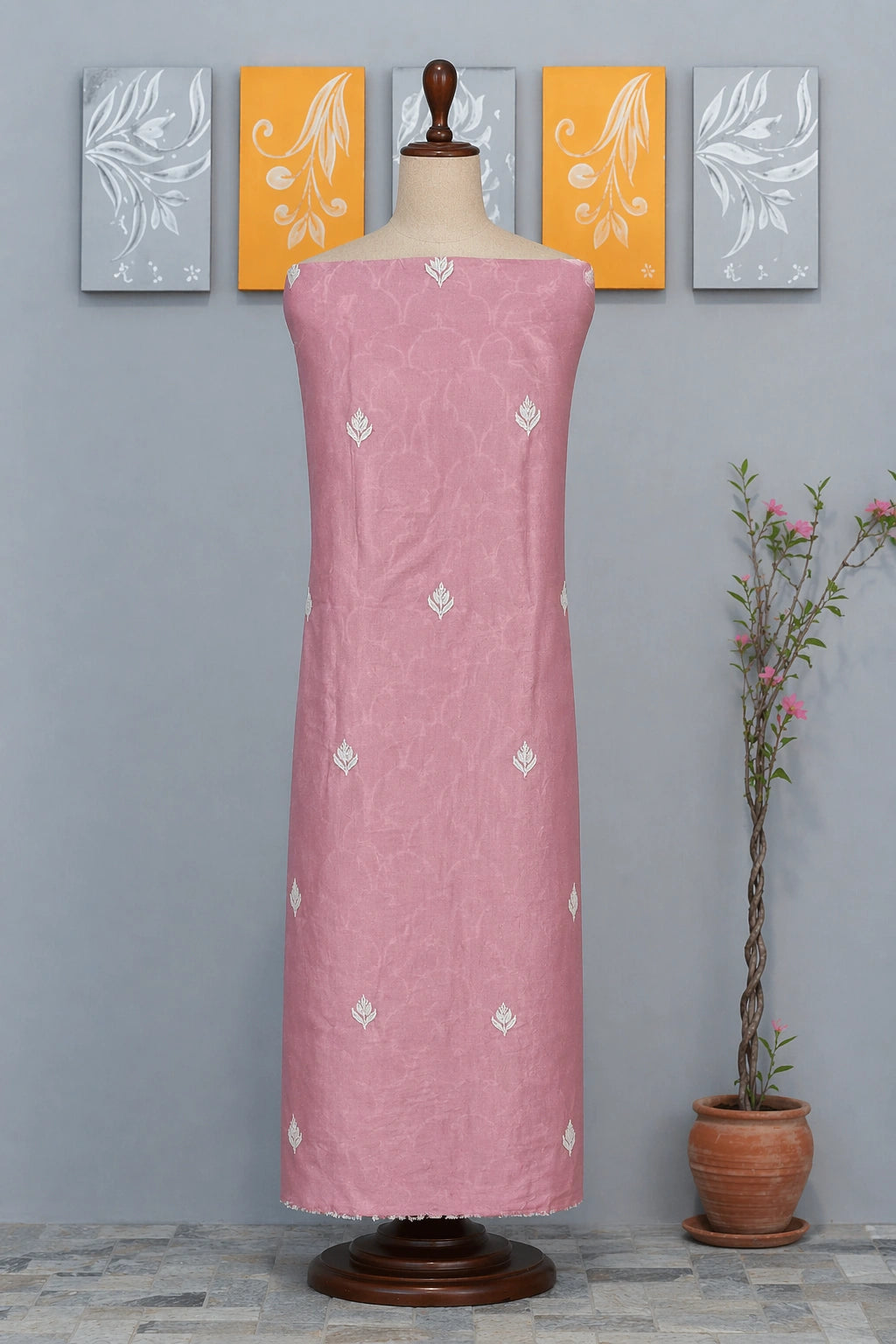 lucknowi chikankari Pink dress on a mannequin against a gray wall with decorative panels and a plant.