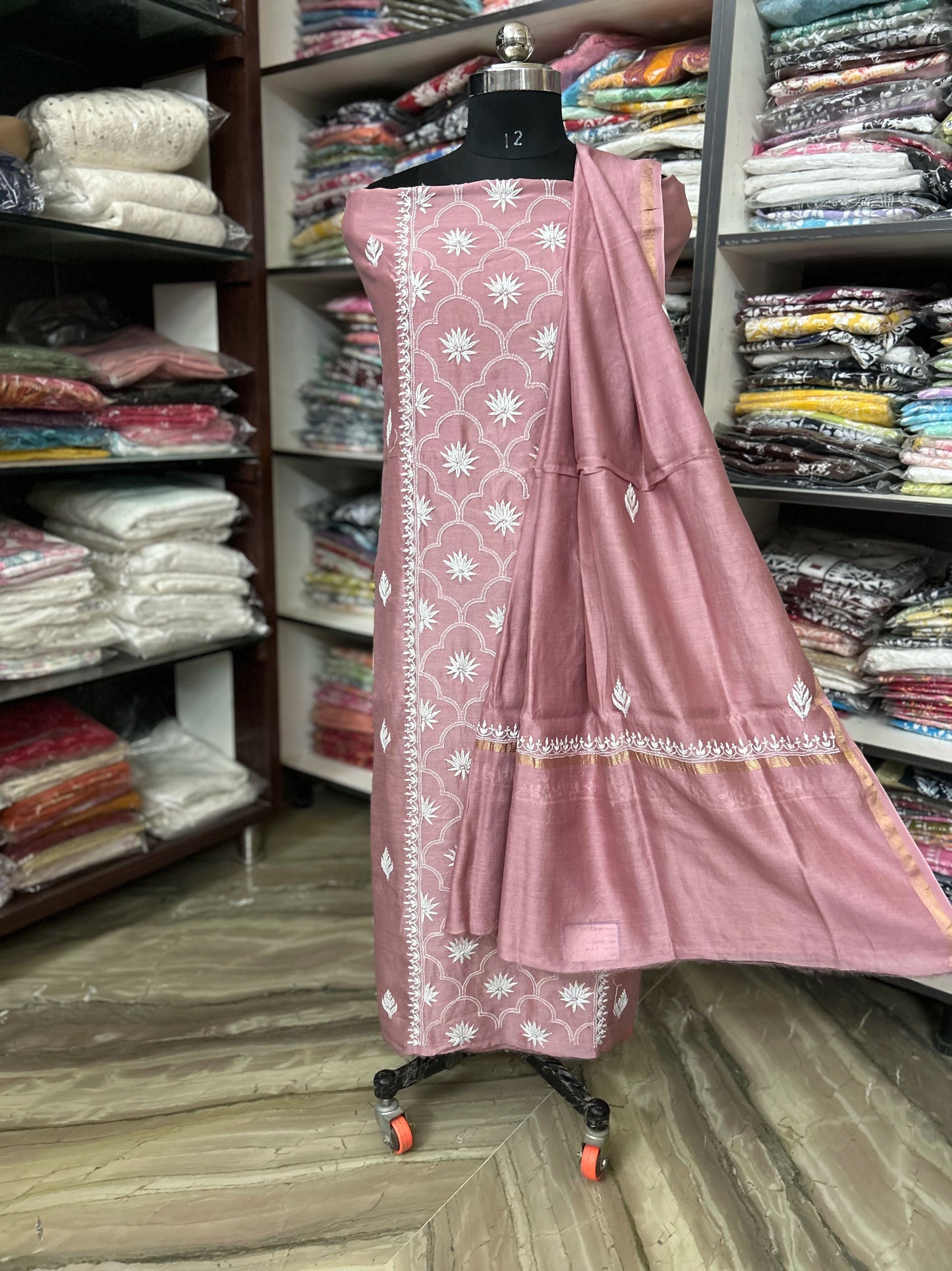 lucknowi chikankari Pink traditional outfit with white patterns on a mannequin in a fabric store.