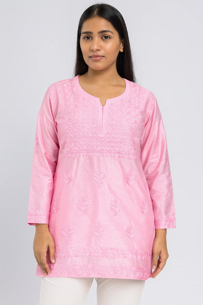 Woman wearing a lucknowi chikankari pink kurta against a plain background