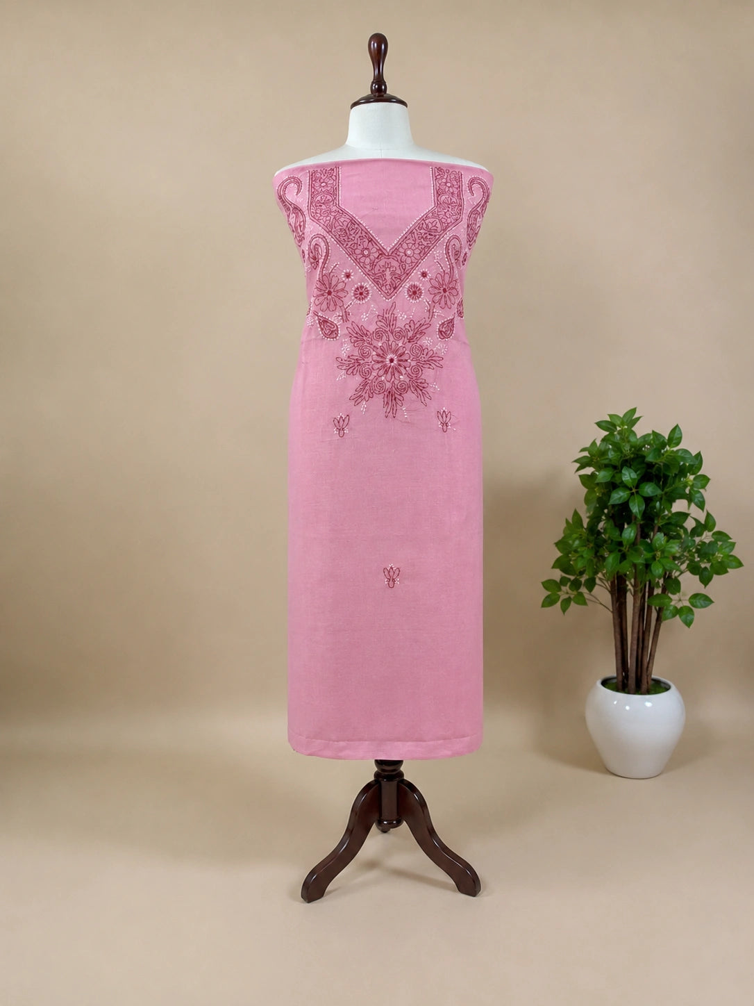 Pink dress with intricate embroidery on a mannequin against a beige background with a plant.