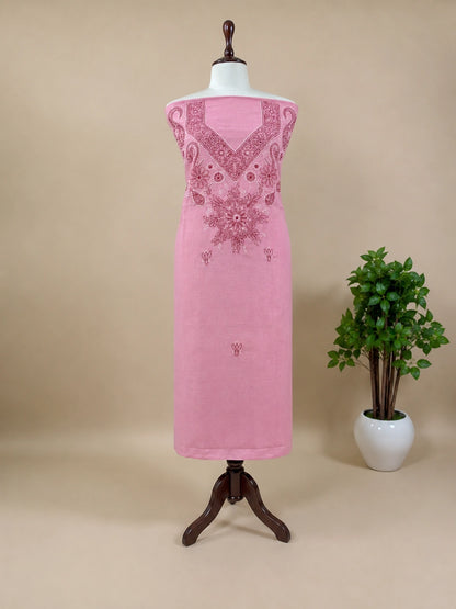 Pink dress with intricate embroidery on a mannequin against a beige background with a plant.