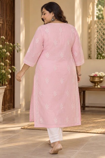 A woman wearing a light pink kurta with white floral embroidery and white pants, photographed from behind in a warm, sunlit indoor setting.
