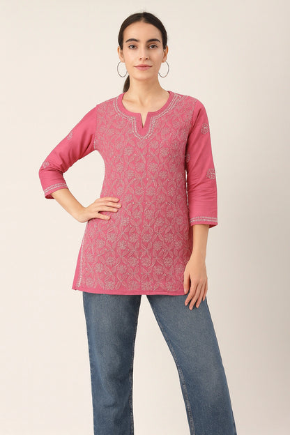 Woman wearing a pink embroidered top and blue jeans on a plain background