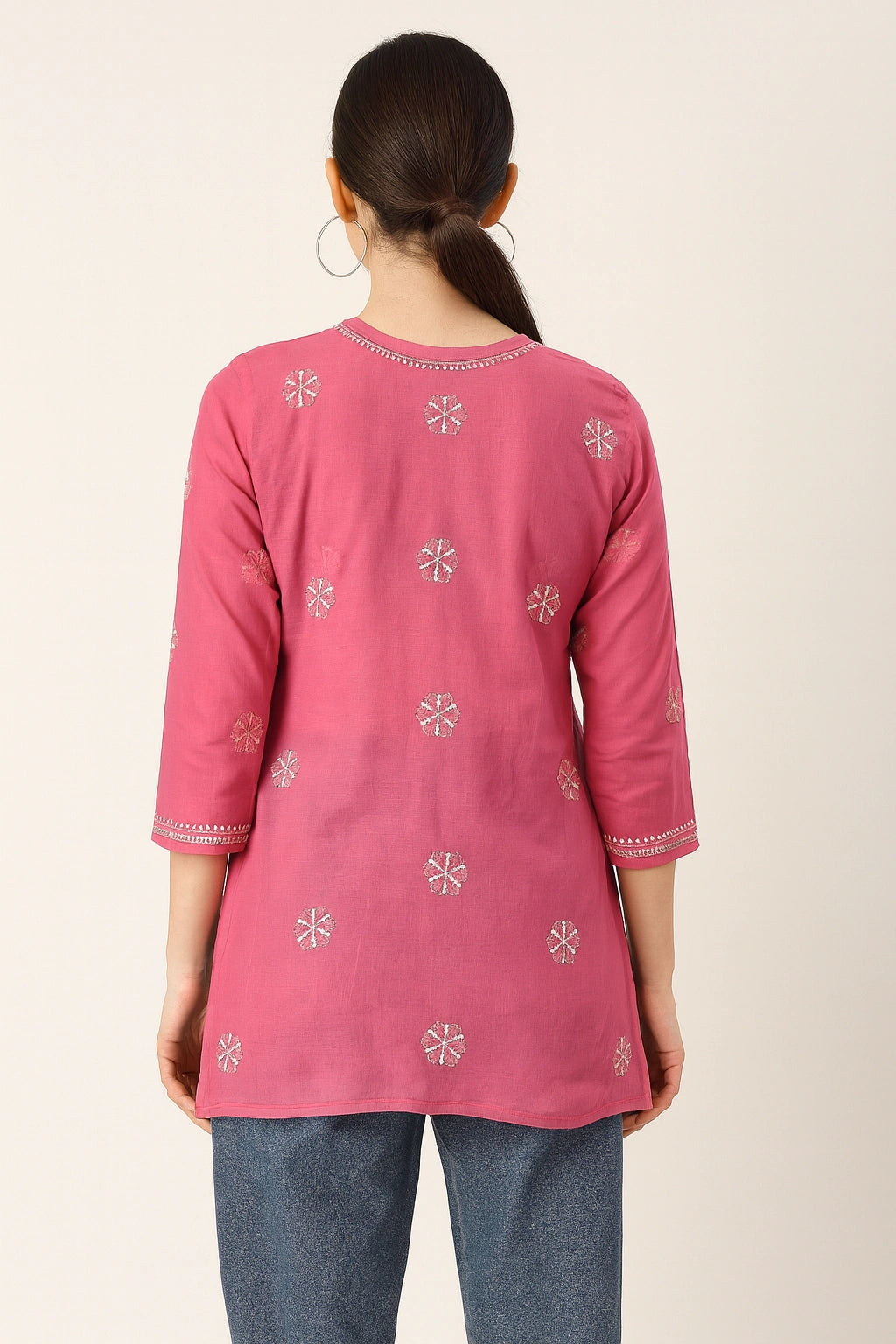 Person wearing a pink embroidered top with blue jeans on a plain background