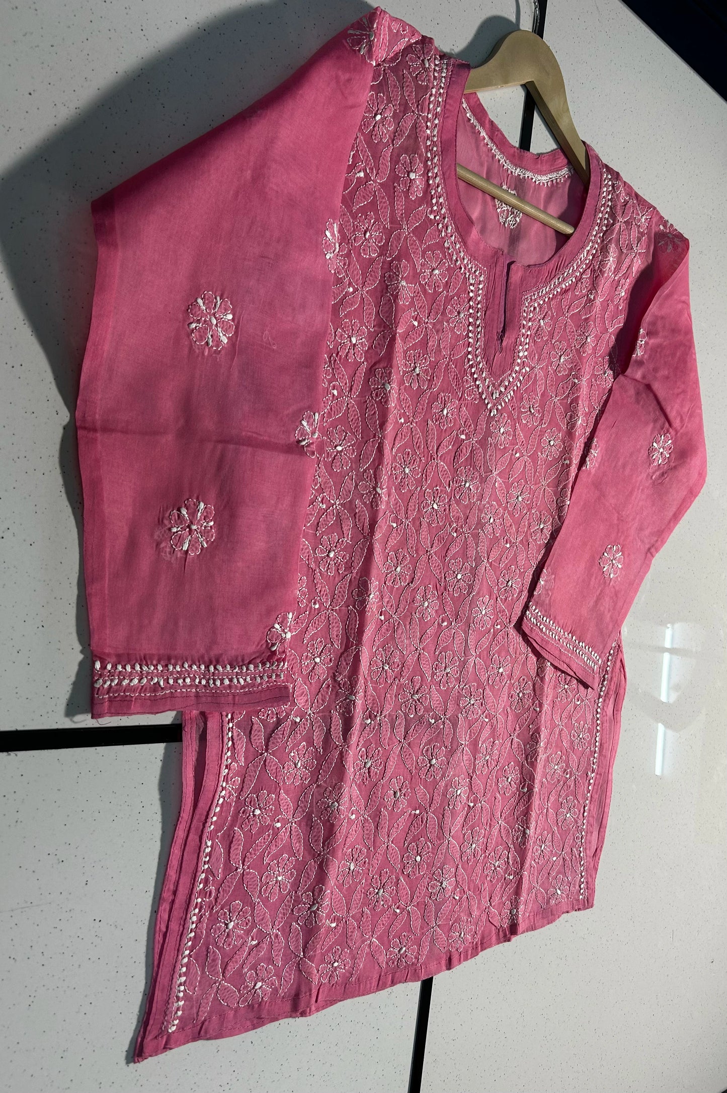 Pink embroidered traditional outfit on a hanger against a white background