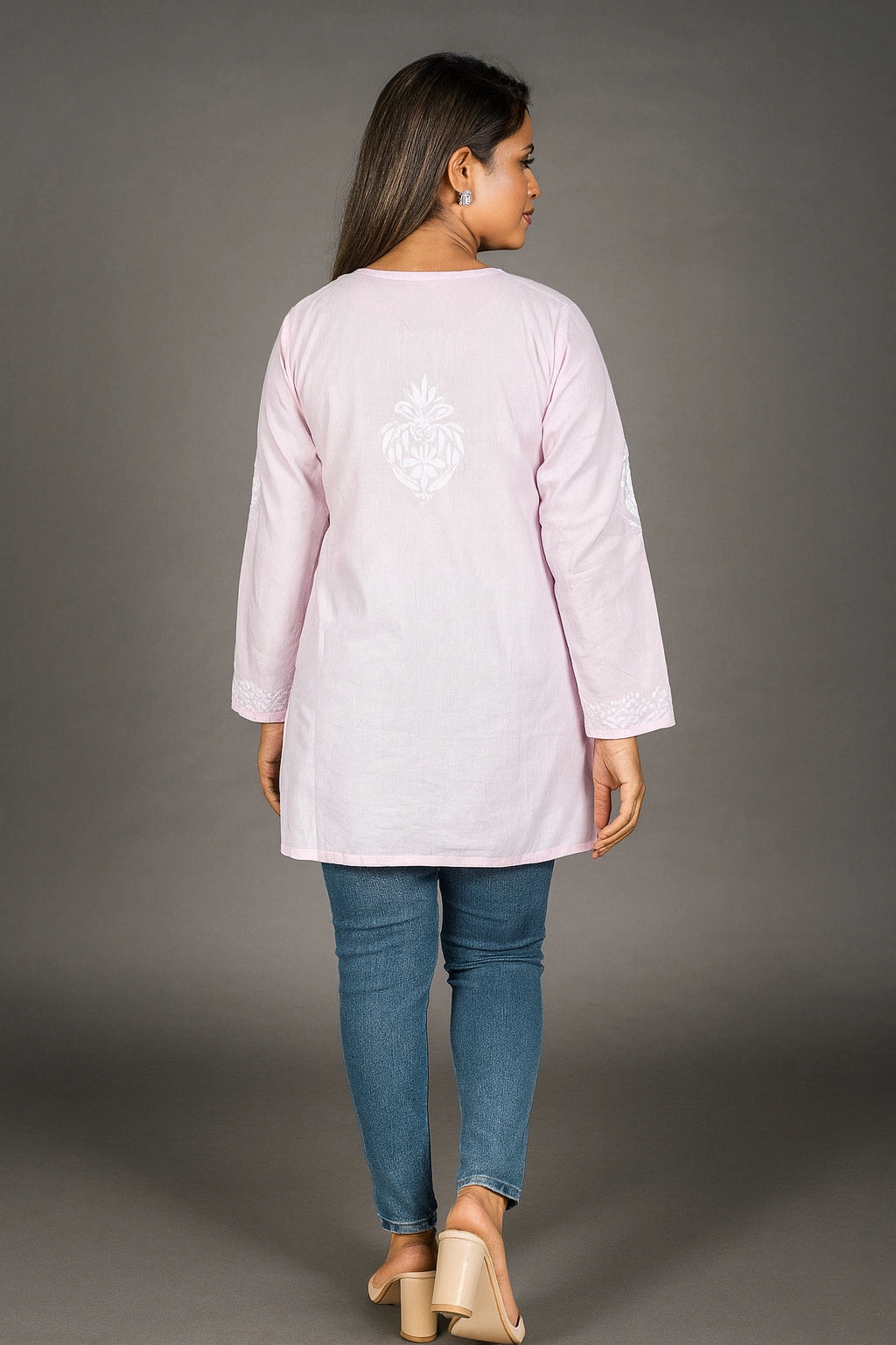 lucknowi chikankari Woman wearing a light pink long-sleeve top with a white design on the back, standing against a gray background.