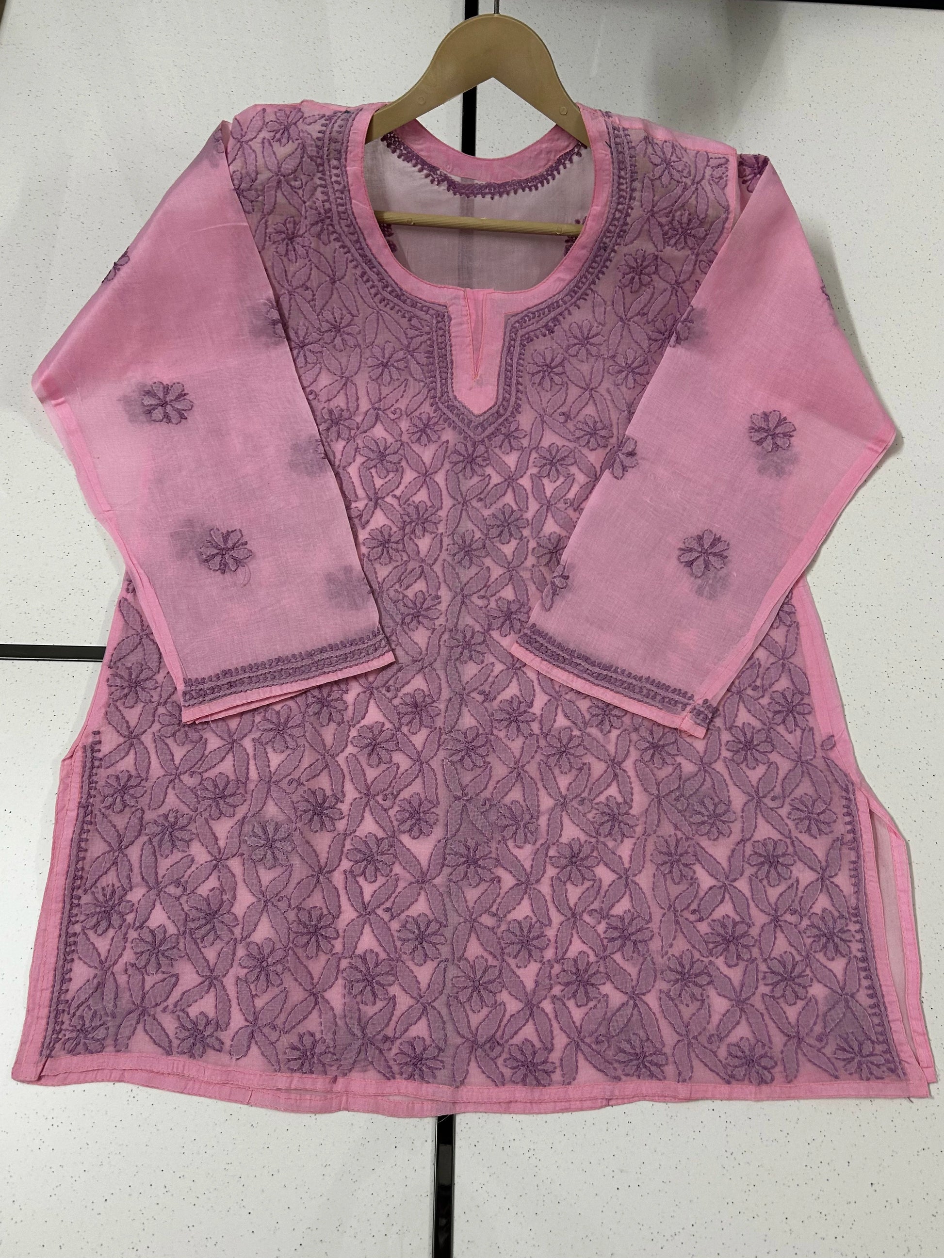 Pink embroidered top on a hanger against a white background