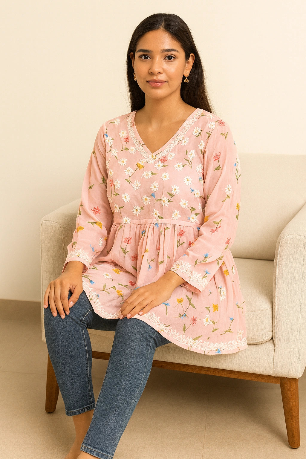 lucknowi chikankari Woman sitting on a chair wearing a pink floral blouse and blue jeans.