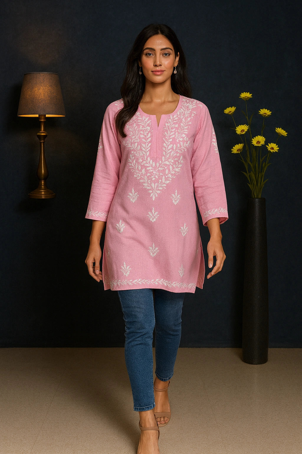Woman wearing a pink embroidered kurta with blue jeans against a dark background