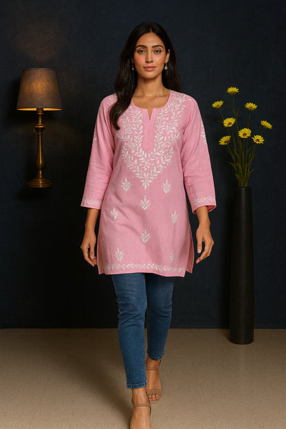 Woman wearing a pink embroidered kurta with blue jeans against a dark background