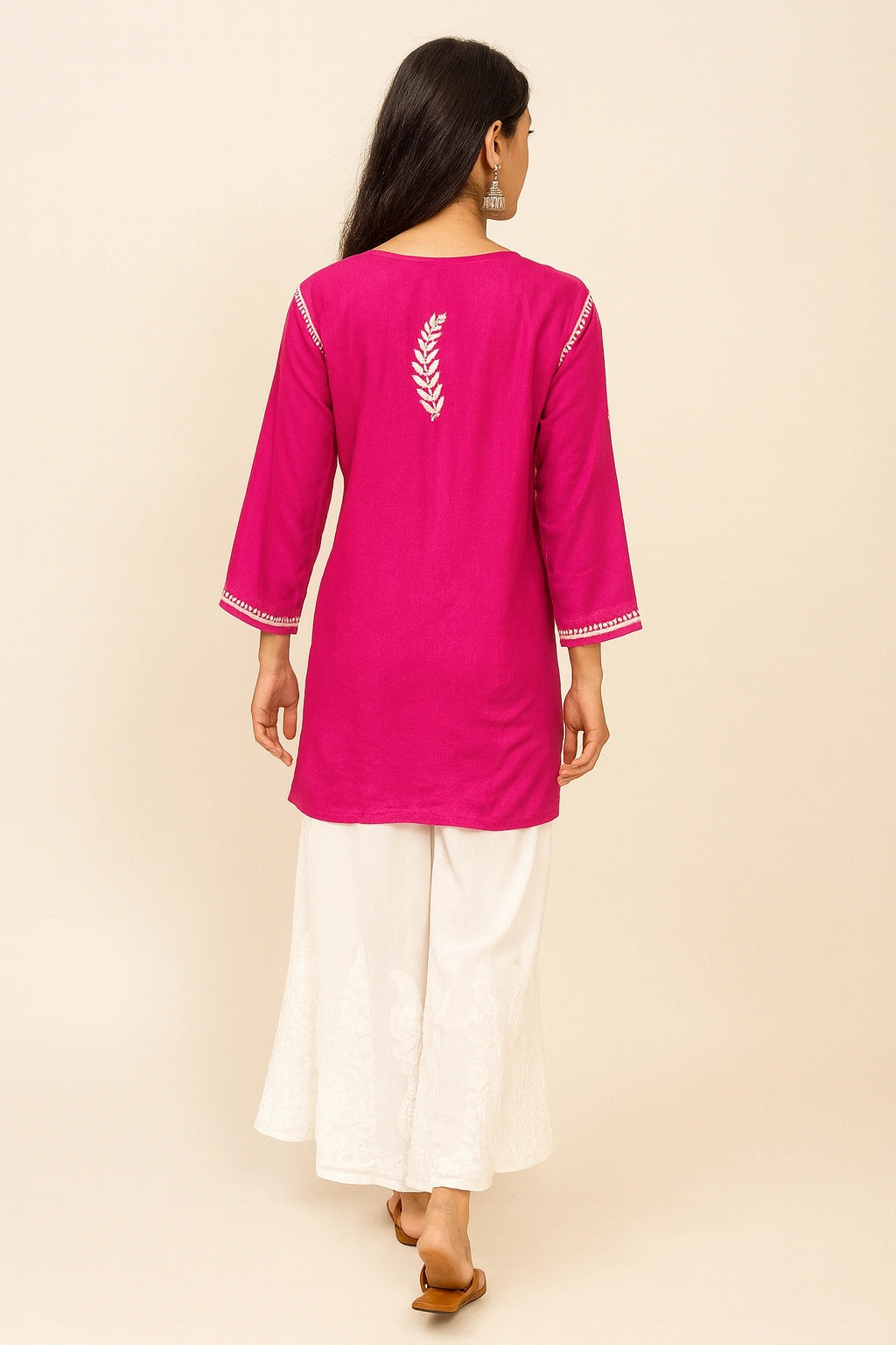 Woman wearing a lucknowi chikankari bright pink kurta with white pants on a beige background