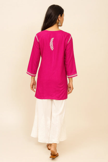 Woman wearing a lucknowi chikankari bright pink kurta with white pants on a beige background