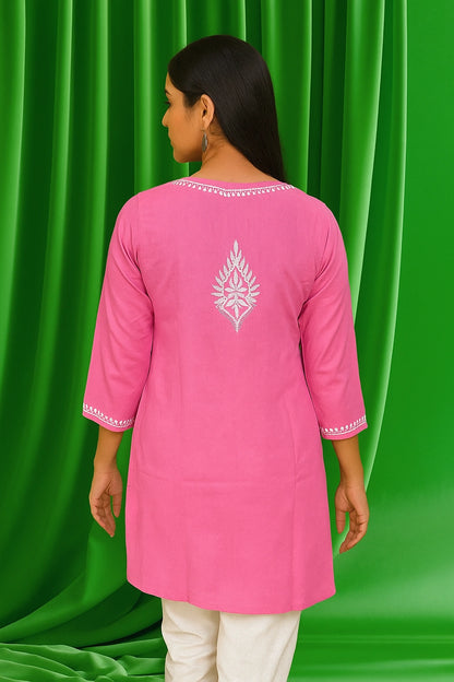 Woman wearing a pink kurta with white embroidery against a green curtain background