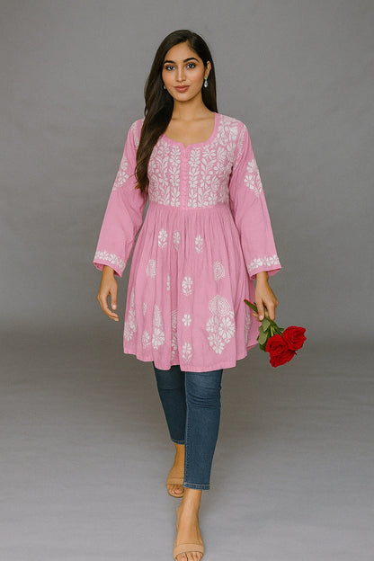 Woman wearing a pink embroidered dress holding a red rose against a gray background