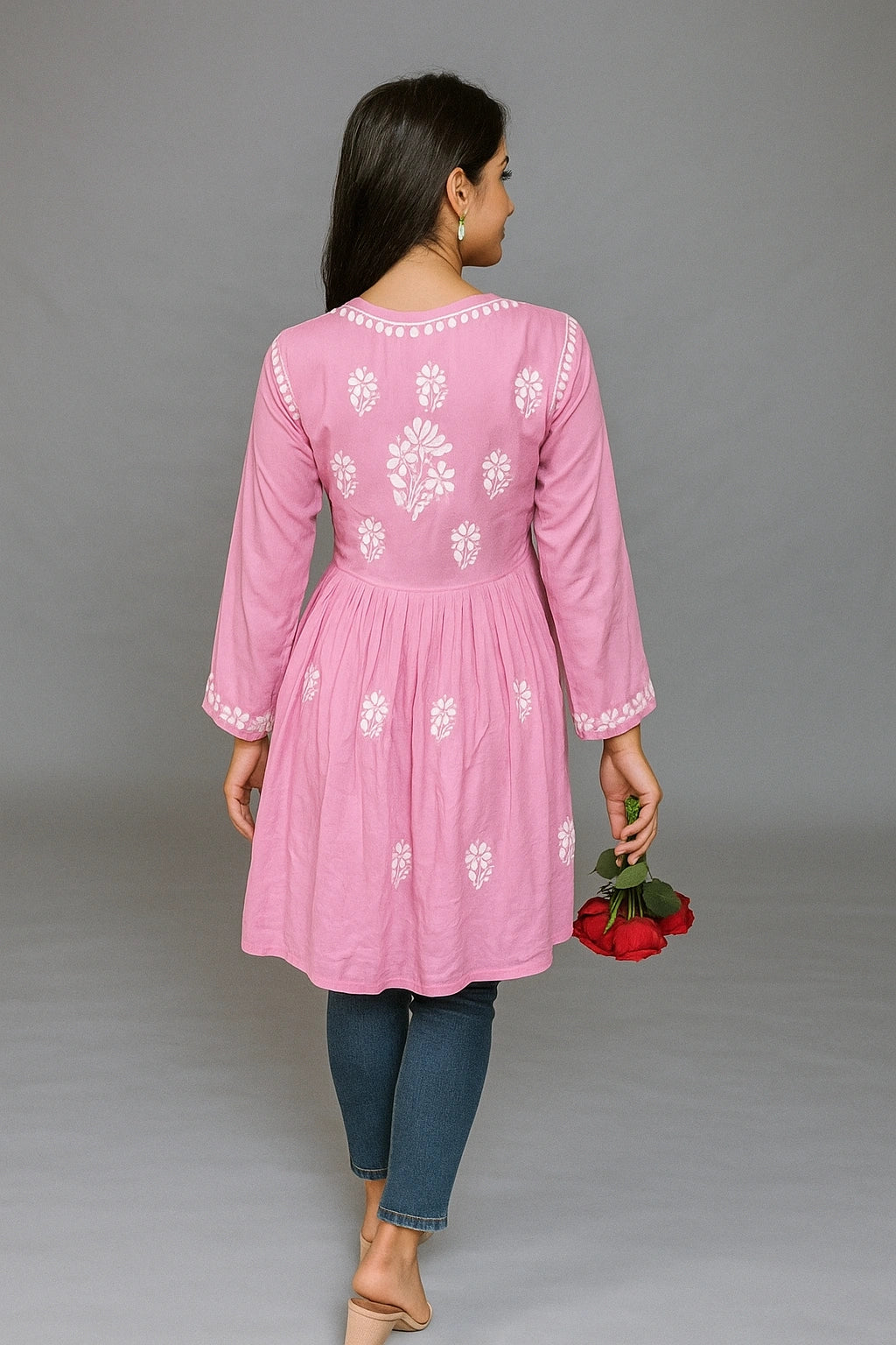 Woman wearing a pink embroidered kurta with blue jeans against a gray background