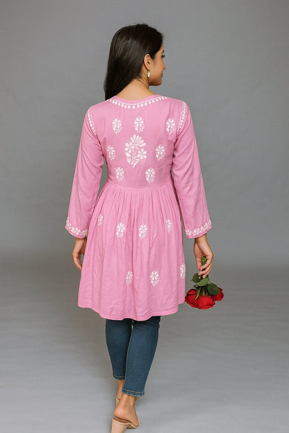 Woman wearing a pink embroidered kurta with blue jeans against a gray background