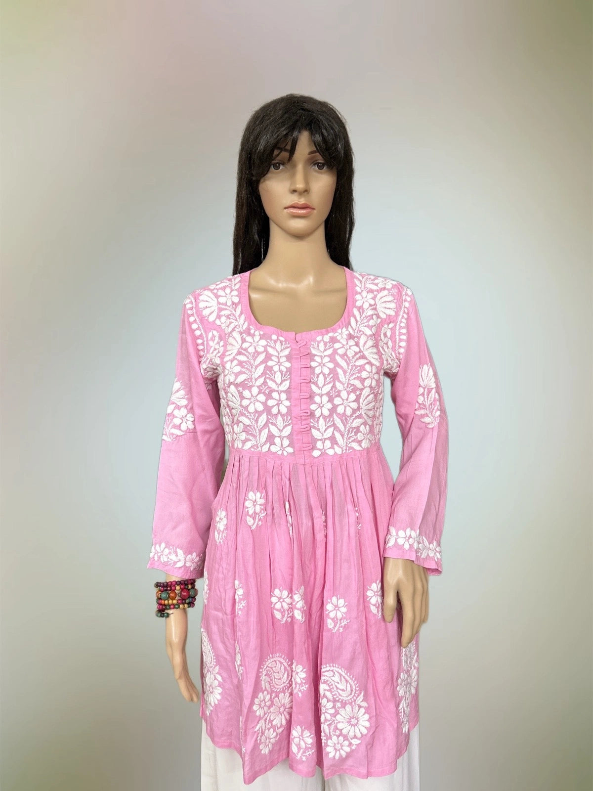 Mannequin wearing a pink dress with white floral embroidery on a plain background