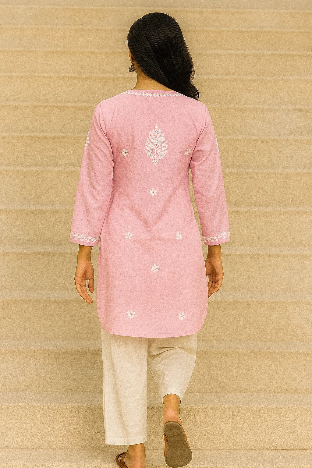 Person wearing a pink embroidered kurta with white pants against a beige wall.