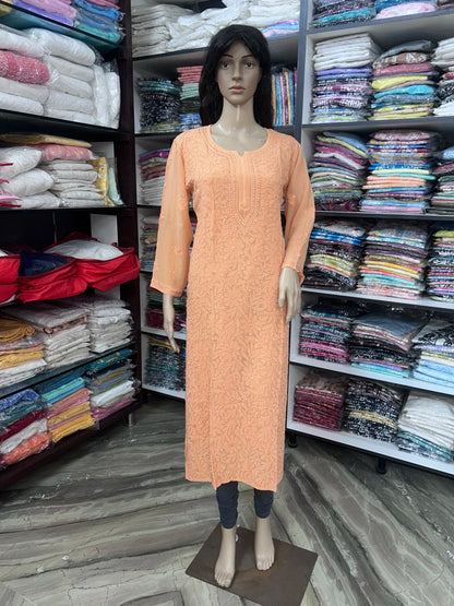 A peach-colored long-sleeve kurta dress displayed on a female mannequin inside a clothing store, with shelves of folded garments visible in the background.