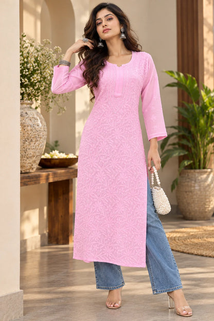 A woman models a Pink embroidered kurta with three-quarter sleeves, paired with light blue jeans, in a styled indoor setting with a stone pedestal and neutral background.