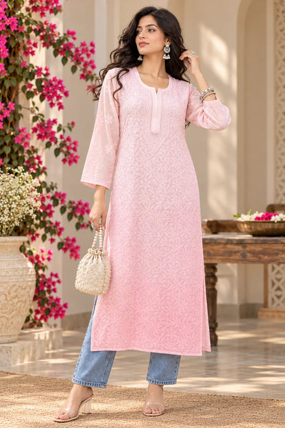 A woman models a light pink embroidered kurta with three-quarter sleeves, paired with light blue jeans, holding a small cream-colored woven handbag in an outdoor courtyard setting.