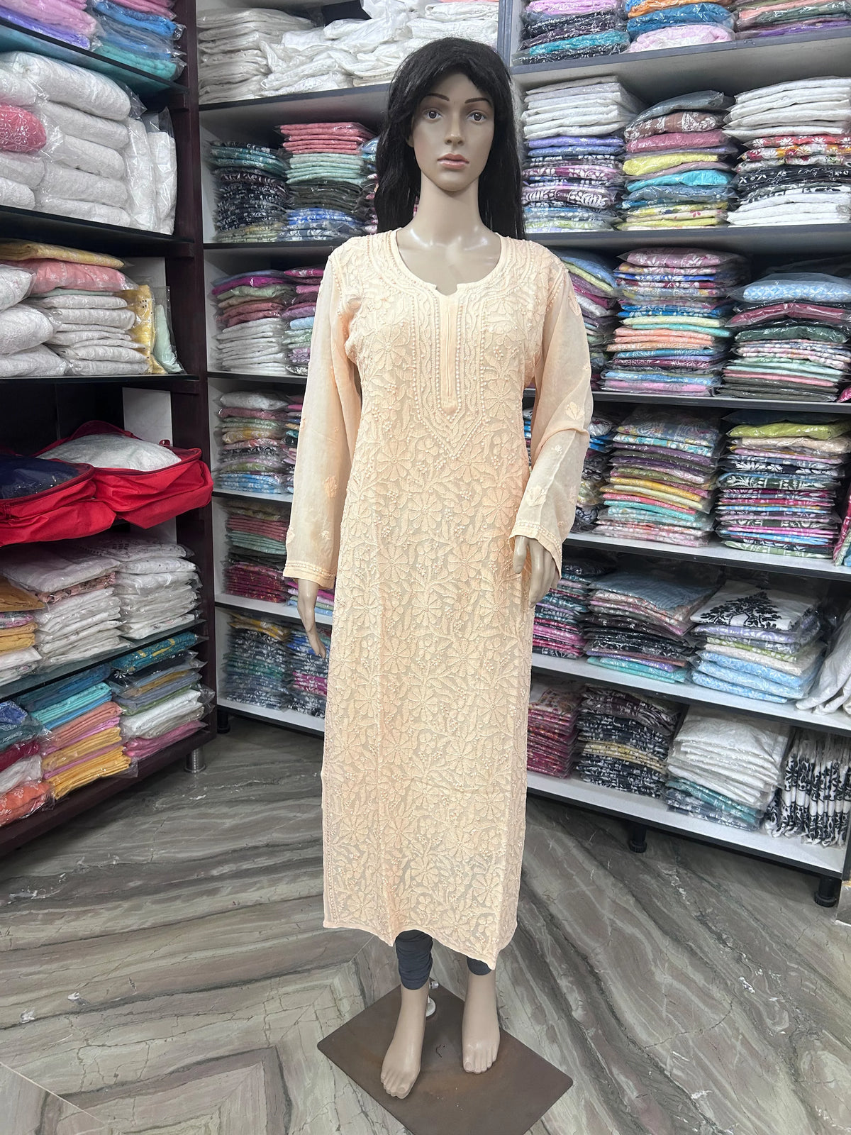lucknowi chikankari A pink long-sleeve kurta displayed on a female mannequin in a clothing store, with shelves of folded fabrics in the background.