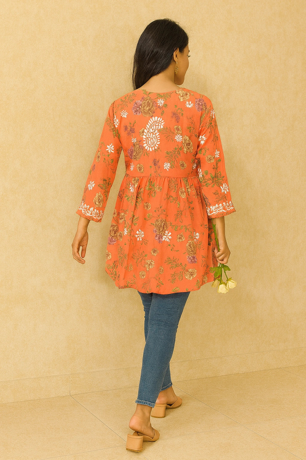 Woman wearing a lucknowi chikankari floral orange dress against a beige background