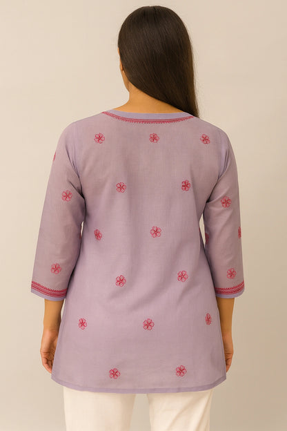 Person wearing a light purple embroidered top with red patterns on a plain background