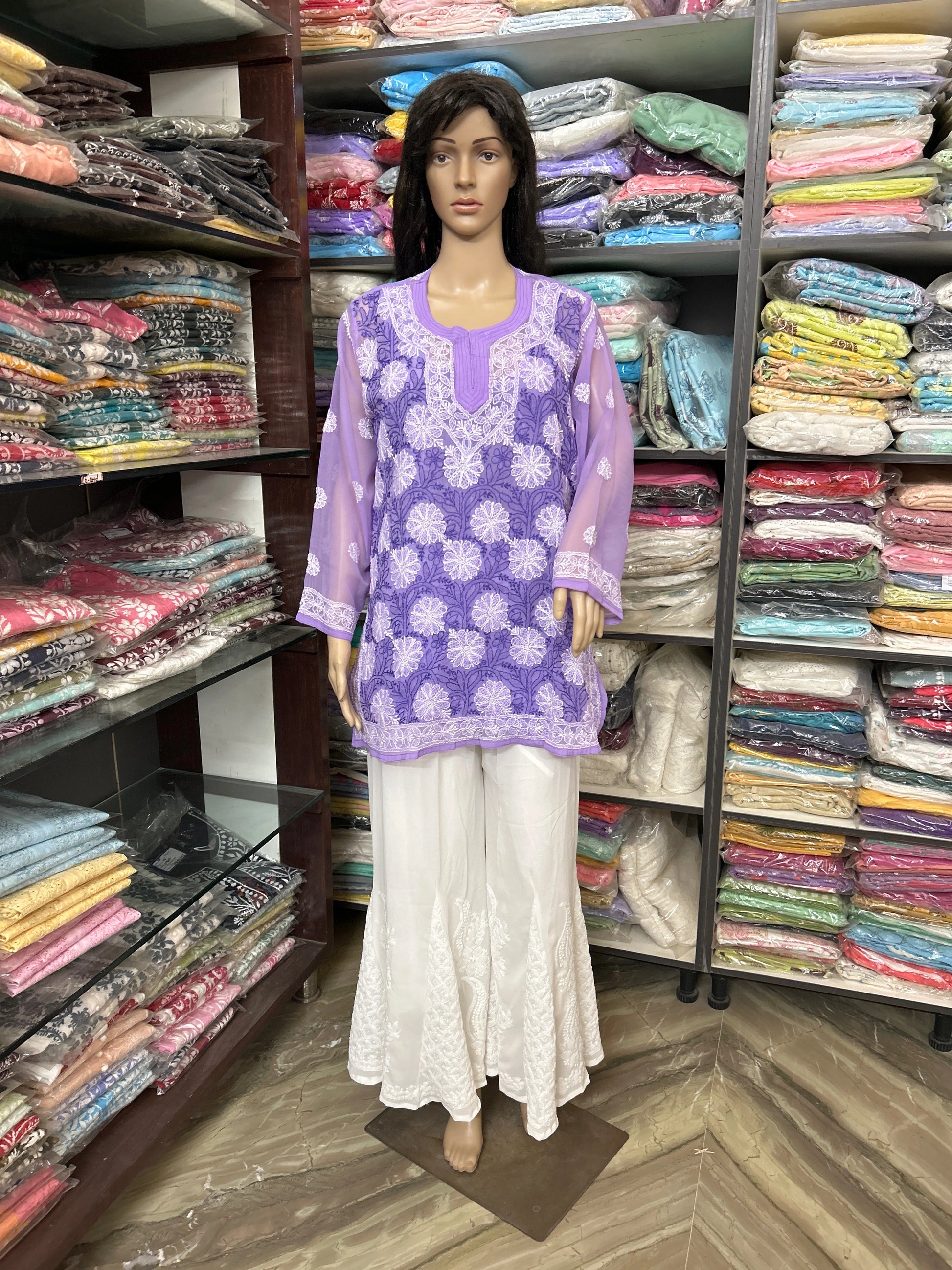lucknowi chikankari Mannequin wearing a purple top and white pants in front of a colorful fabric display.
