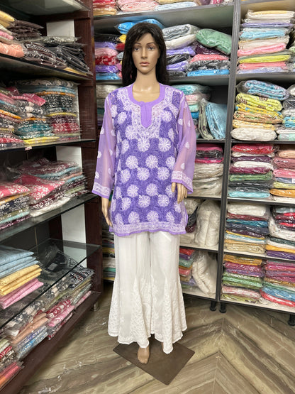 lucknowi chikankari Mannequin wearing a purple top and white pants in front of a colorful fabric display.