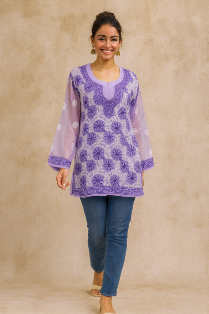 Woman wearing a purple embroidered top and blue pants against a beige background