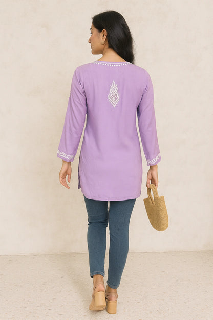 Woman wearing a light purple embroidered kurta with blue jeans against a beige background