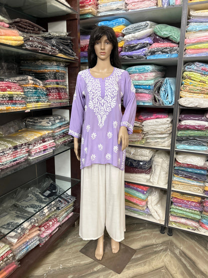 lucknowi chikankari Mannequin wearing a purple top and beige pants in a fabric store with shelves of colorful fabrics.