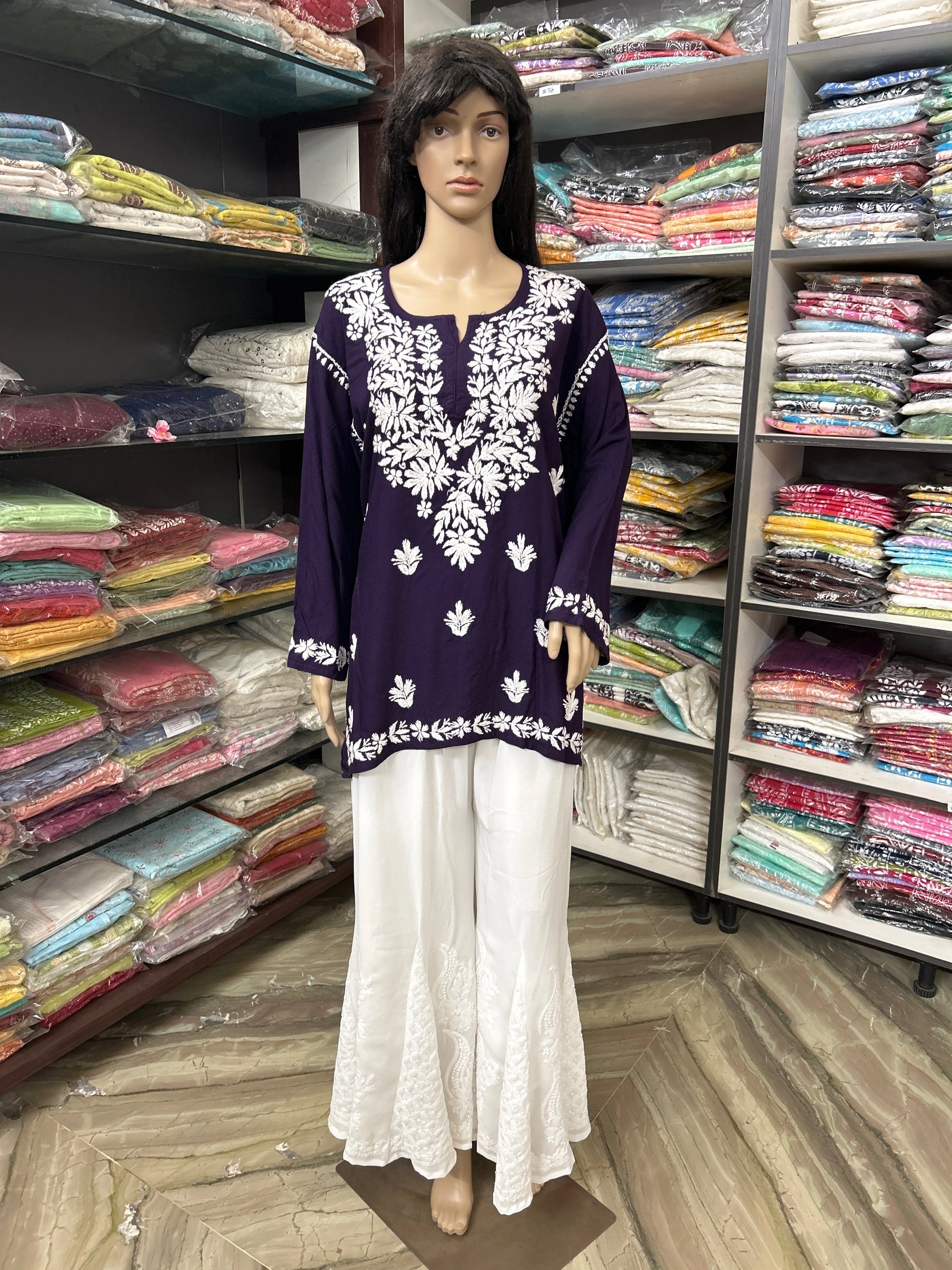 Mannequin wearing a purple embroidered top and white pants in a fabric store.