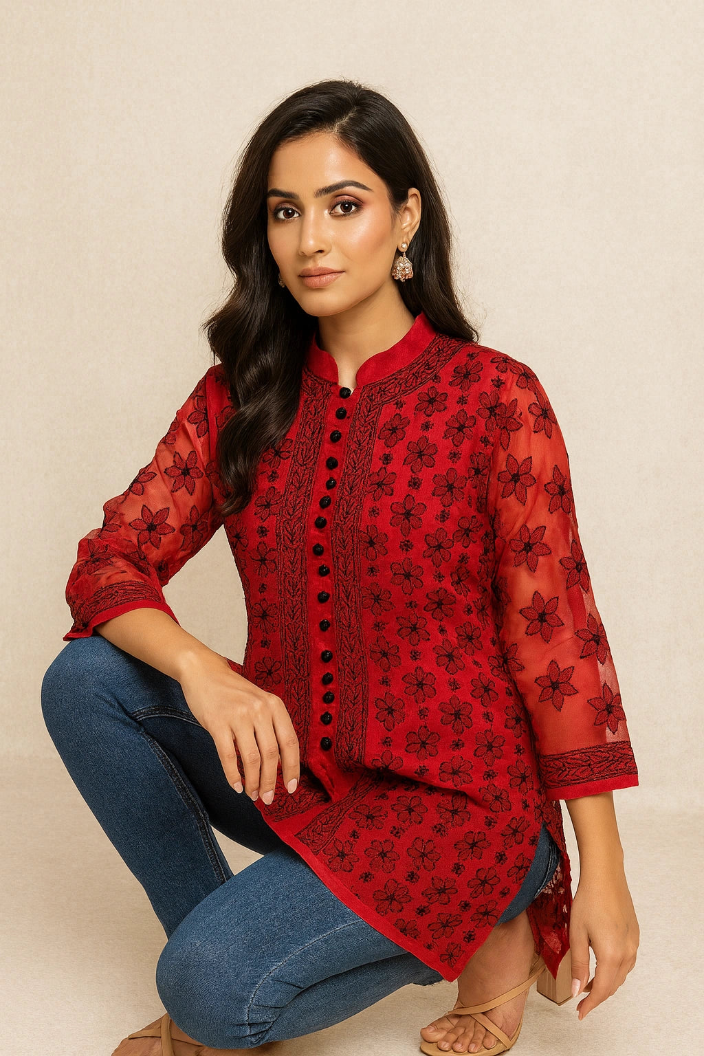 Woman wearing a lucknowi chikankari red floral blouse with blue jeans on a beige background