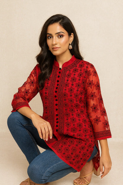 Woman wearing a lucknowi chikankari red floral blouse with blue jeans on a beige background